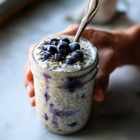 A hand holding a jar of yogurt with blueberries.
