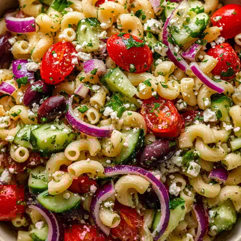 A bowl of Greek pasta salad with tomatoes, cucumbers, and feta cheese.